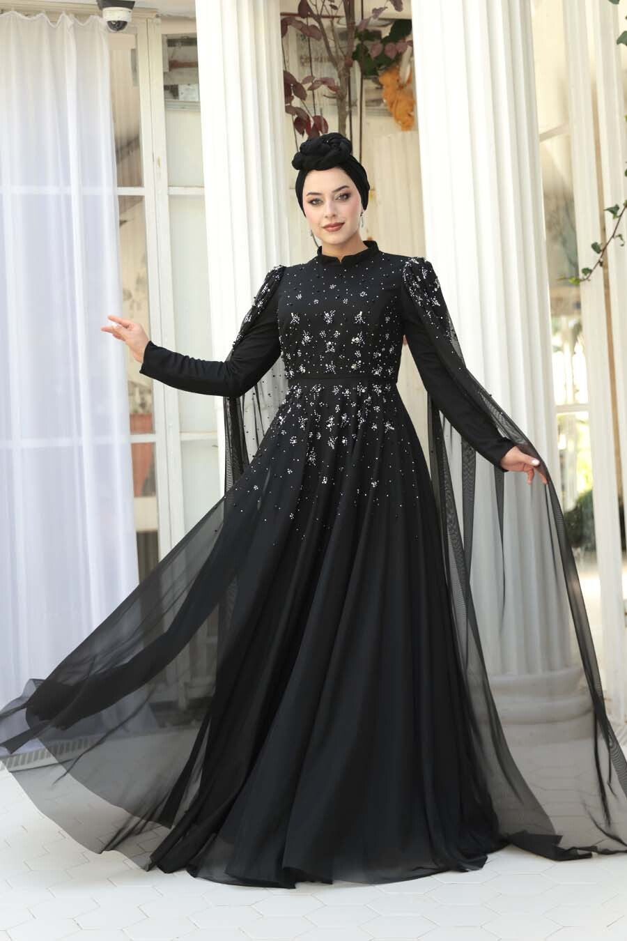 Woman wearing a black evening gown with long sleeves and a flowing skirt in an indoor setting.