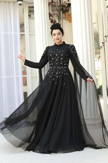 Woman wearing a black evening gown with long sleeves and a flowing skirt in an indoor setting.